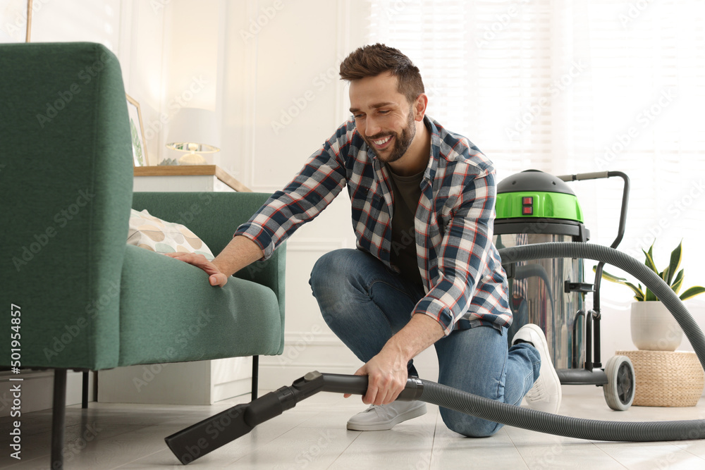 Canvas Prints Man vacuuming floor under sofa in living room