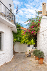 Fototapeta na wymiar A picturesque street of stone and whitewashed homes, pink flowers, and a sidewalk cafe in the picturesque village of the small Greek island of Hydra, Greece.