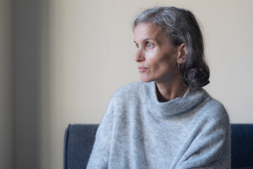 Close up of seated middle aged woman in grey sweater looking annoyed (selective focus)