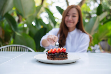 Blurred image of a beautiful young asian woman eating a piece of strawberry chocolate cake