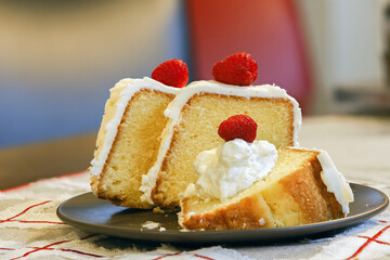 Almond cake baked traditionally in a bundt pan, sliced and served with whipped cream and a raspberry.