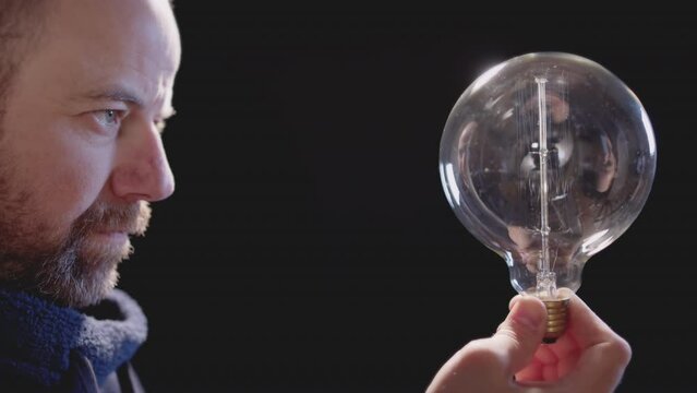 Man holding light bulb against black background that loses energy. Concept of global energy crisis