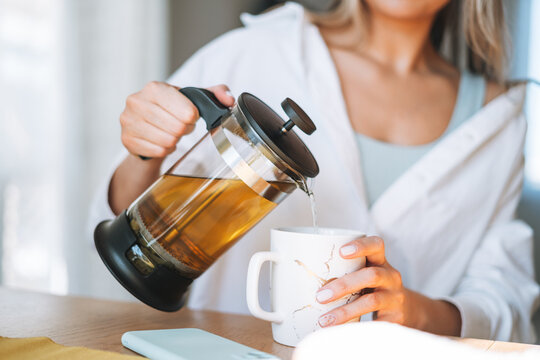 Crop photo of Young woman with blonde long hair in white shirt drinking tea on dinner table in bright interior at the home