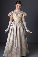 Fototapeta premium A Victorian woman wearing a gold evening gown with long, lace, fingerless gloves and standing against a studio backdrop