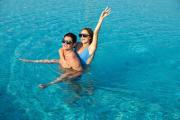 piggyback ride on the back. happy young couple by the pool. couple are relaxing at swimming pool...