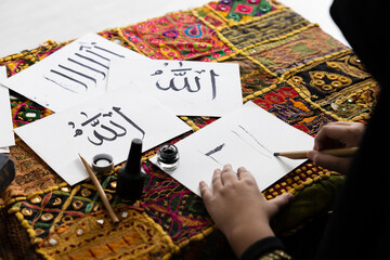 close up muslim girl hands writing Arabic text with bamboo pens and black ink on paper, Arabic letters mean the name of Muslim god "Allah"