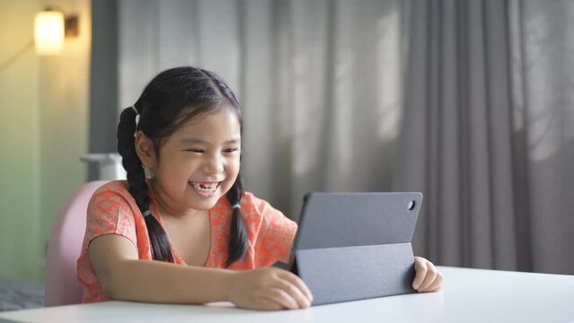 Asian child happy smile talking fun to teacher via video call learning on computer tablet or kid girl student enjoy speaking studying on study online class or person learn from home school in bedroom