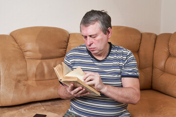 An elderly man is reading a book while sitting on the couch - 501979665