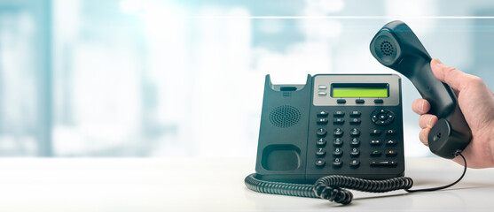 Fototapeta Dialing telephone keypad concept for communication, contact us and customer service support. black office voip phone with handset up on table on blurred office background. banner obraz