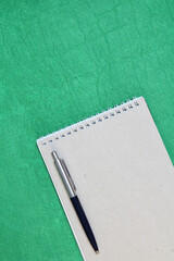 White and gray notepad sheet with spiral with pen against the background of green fabric. Concept of analysis, study, attentive work. Stock photo with empty place for your text and design. Vertical