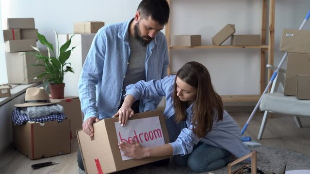 young couple prepare personal stuff relocating to first own house, sealing cardboard boxes with belongings on moving day to new apartment. woman sticking a piece of paper on a box. Life changes