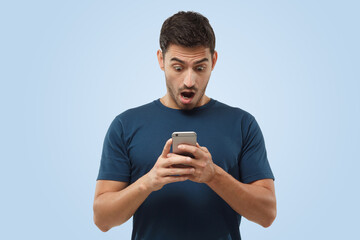 Excited attractive young man in blue t-shirt, holding smartphone, looking confused