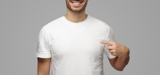 Young man pointing with index finger at blank white t-shirt with empty space