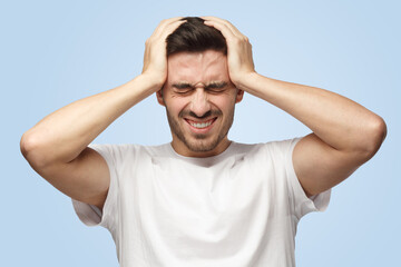 Attractive young European Caucasian man pressing hands to temples experiencing headache