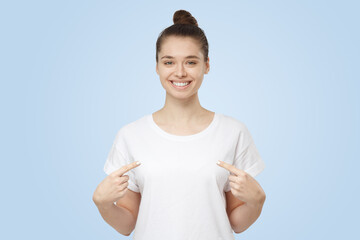 Smiling young woman pointing at her blank white t-shirt with both index fingers
