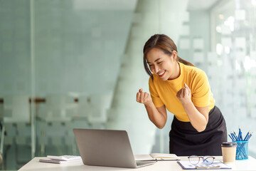 Successful young Asian business woman achieving goals excited raised hands rejoicing with laptop in...