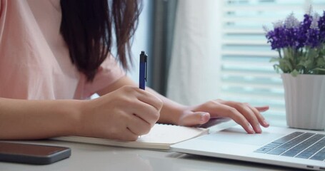 An woman Asian university college student uses a laptop computer on the table at his home.Female hands using a laptop and take notes on notepad.for studying online.Online education concept. - Powered by Adobe