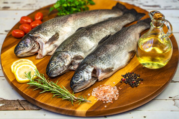 Three raw trout with spices and olive oil on a wooden board.