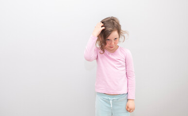 Child, Caucasian 6 years old, in a pink coat on a gray background. The child in thought scratches his head with his hands, emotions on his face.