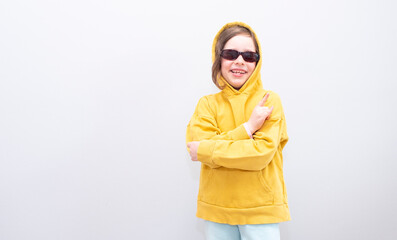 Child, Caucasian 6 years old, in a yellow sweatshirt with a hood and sunglasses on a gray background. Emotions on her face and crossed her arms on the gruli and hand gesture 