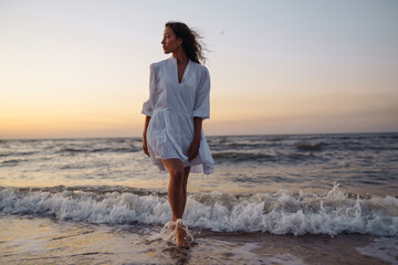 Stylish woman in elegant white dress posing near the sea. Summer time. Travel, weekend, relax and lifestyle concept.