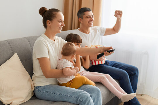 Portrait of attractive lovely positive glad family wearing casual white t-shirts jeans sitting on sofa having fun watching funny video enjoying, spending free time.