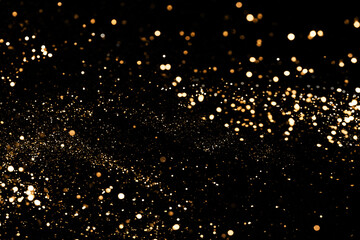 Black festive background. Abstract scattering of gold sparkles on black. Holiday backdrop, selective focus