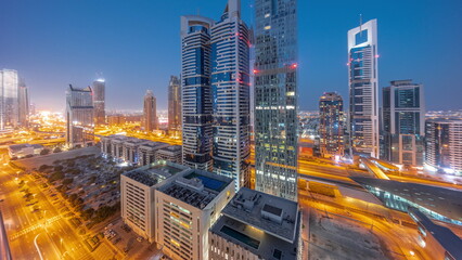 Naklejka na ściany i meble Aerial view of Dubai International Financial District with many skyscrapers night to day timelapse.