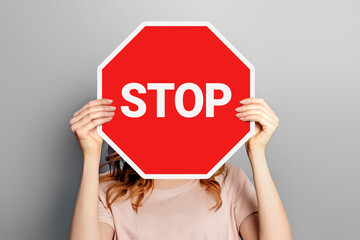 Woman holding poster with stop sign in hands covering her face isolated on grey background