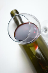 A glass of red wine with an empty bottle on a white background. Excessive alcohol consumption.
