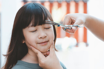 Women's hands to cut the front hair or bangs for a cute Asian girl at home. Mothers are happy to cut their children's hair. Hair care concept