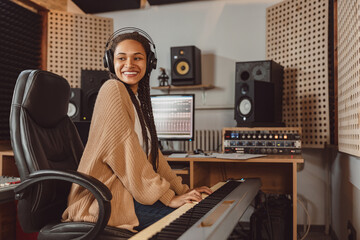 Attractive stylish African American female musician sound engineer playing synthesizer while...