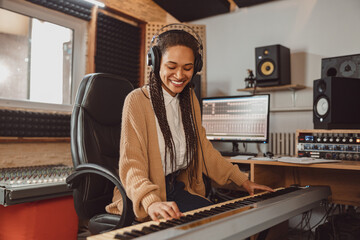 Stylish woman musician, sound composer playing synthesizer and rehearsing new song in the modern recording music studio - obrazy, fototapety, plakaty
