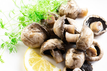 On a white isolated background, a plate dish with marinated whole champignon mushrooms, fresh lemon and dill