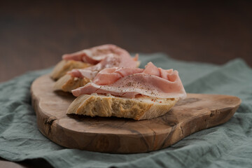 Toassted baguette slices with prosciutto cotto and cream cheese on olive wood board