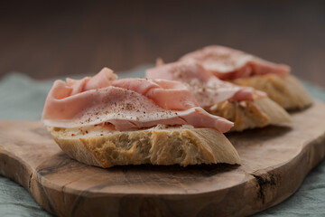 Toassted baguette slices with prosciutto cotto and cream cheese on olive wood board