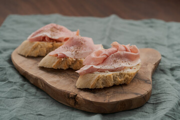 Toassted baguette slices with prosciutto cotto and cream cheese on olive wood board