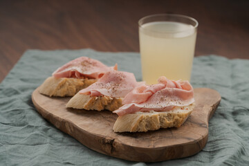 Toassted baguette slices with prosciutto cotto and cream cheese on olive wood board with lemonade
