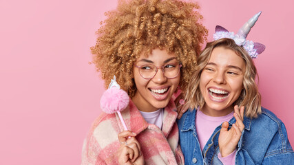 Horizontal shot of happy female friends have fun smile toothily laugh positively dressed in...