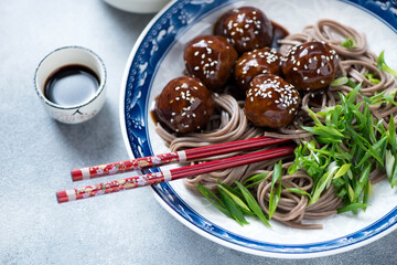 Close-up of pork meatballs in teriyaki sauce with soba noodles and scallions, selective focus, horizontal shot