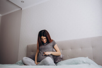 Obraz premium Enjoying Pregnancy. Pregnant Lady Touching Belly Smiling Sitting On Bed At Home In Morning. Free Space