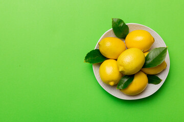 Fresh cutted lemon and whole lemons over round plate on colored background. Food and drink ingredients preparing. healthy eating theme top view vith copy space