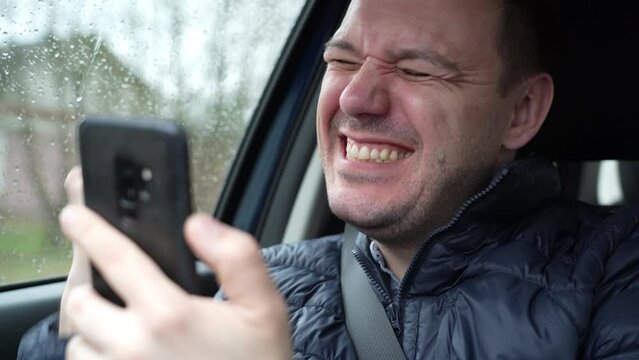 Happy excited millennial man looking at smartphone screen and showing yeah gesture in car