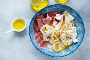 Blue bowl with italian pappardelle, prosciutto, ricotta and poached egg, above view on a light-blue...