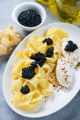 White oval plate with italian pappardelle, black caviar and cream-cheese, closeup, vertical shot