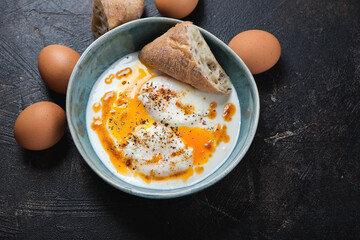 Bowl of turkish poached eggs served with yogurt and melted spicy butter, elevated view on a dark-brown stone background, horizontal shot