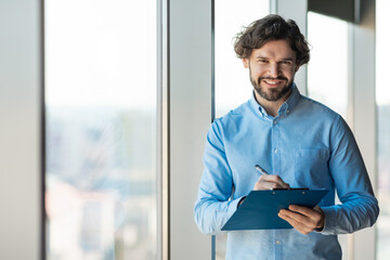 Fototapeta premium Portrait of confident man looking at camera writing in clipboard