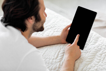 Young millennial guy using digital tablet in bed, mockup