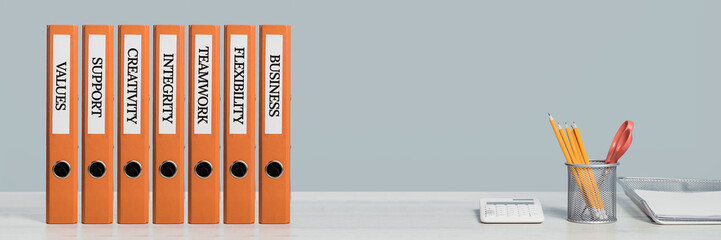 A row of business strategy and teamwork orange document binders or lever arch file with paperwork on an office shelf or desk. Calculator and pencils. Business concept wide banner. Copy space