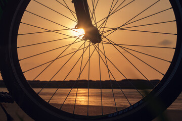 Close-up silhouette of a bike wheel at sunset. The sun shines through the wheel of a bicycle, selective focus